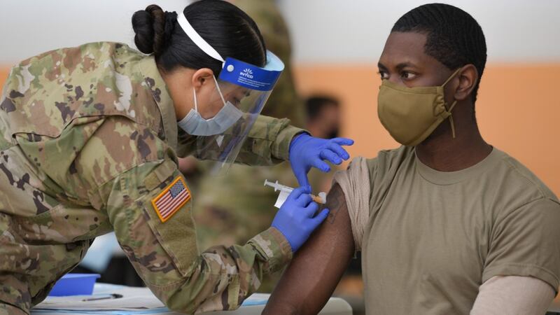 U.S. Army Spc. Eyza Carrasco, left, with 2nd Cavalry Regiment, administers a COVID-19...